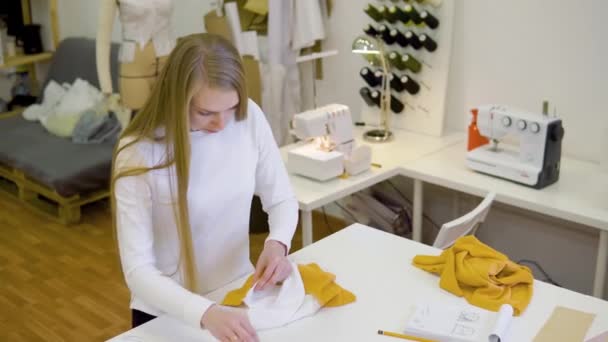 Mujer con el pelo rubio freelancer, diseñador de moda o sastre que trabaja en un diseño o proyecto con telas de colores en el taller. Vista frontal — Vídeo de stock