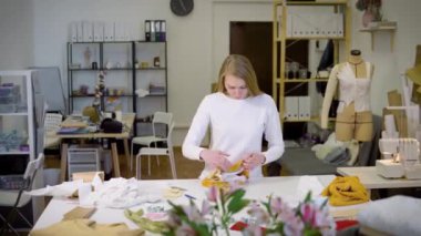 Sarışın bir kadın, serbest çalışan, moda tasarımcısı ya da atölyede renkli kumaşlarla tasarım ya da taslak üzerinde çalışan bir terzi. Ön görünüm