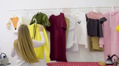 Kadın moda tasarımcısı yeni kadın giyim koleksiyonu üzerinde çalışıyor. Stüdyo atölyesi, terzi, terzi ya da nakışçı. Elbise rafının yanında şık el yapımı kıyafetlerle duruyor.