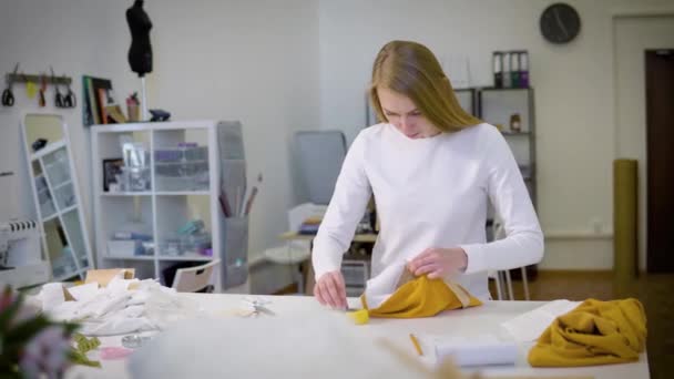 Frau mit blonden Haaren - Freiberuflerin, Modedesignerin oder Schneiderin, die in der Werkstatt an einem Entwurf oder Entwurf mit bunten Stoffen arbeitet. Frontansicht — Stockvideo