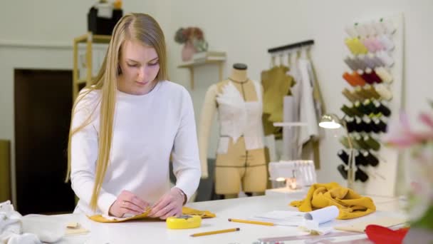 Kvinna med blont hår - frilansare, modedesigner eller skräddare arbetar på en design eller utkast med färgglada tyger i verkstad. Framifrån — Stockvideo
