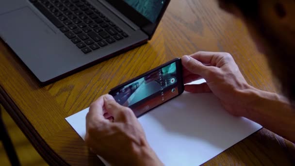 Een jongeman maakt een video over een laptop met papier als schuifregelaar. Life hack voor video schieten — Stockvideo