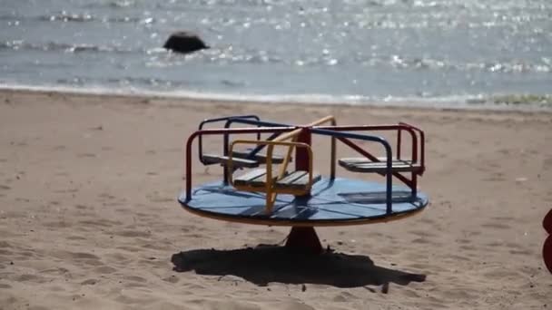 Детская карусель вращается сама по себе на фоне голубой воды на пляже. Лето 2015 года, Россия, Санкт-Петербург, Full HD — стоковое видео