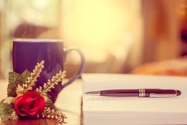 Caneta no caderno e xícara de café, flor . Fotografia De Stock