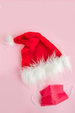 Pembe arka planda yüz maskesi olan Noel Baba şapkası, Coronavirus salgını sırasında Noel 'i kutlayan minimum konsept. Sosyal medya için dikey, düz