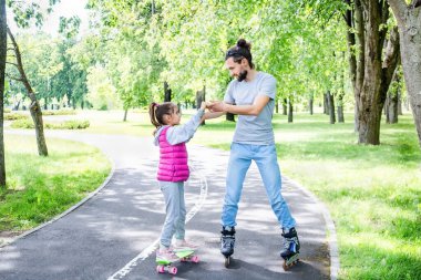 Parkta aile aktiviteleri. Mutlu baba küçük kızına parkta paten kaymayı öğretiyor. İyi bir baba çocuğuyla vakit geçirir..