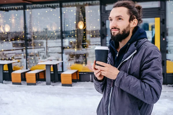 Lifestyle morning coffee at the city concept. Portrait of cheerful attractive bearded man enjoying hot coffee, looking side outdoors. copy space