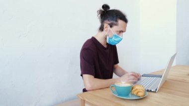 Yeni normal yaşam tarzı konsepti. Koruyucu yüz maskesi takan serbest çalışan bir adam dizüstü bilgisayar kullanıyor ve kafede çalışıyor..