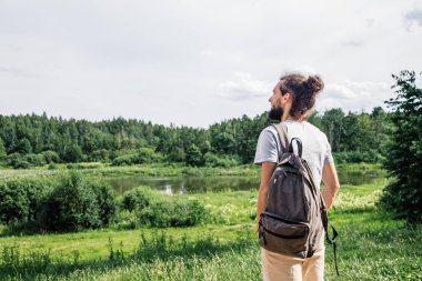 Genç adam yaz doğasının tadını çıkarıyor. Sırt çantalı sakallı adam manzaraya bakıyor..