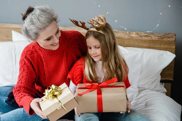 Családi karácsonyi koncepció. Vidám nagymama és az aranyos unokája ajándékot cserélnek. Család ajándékokkal a szobában. Jogdíjmentes Stock Képek