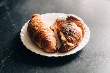 Avrupa kahvaltısı konsepti. Kremalı kruvasanlar beyaz tabakta ve siyah arka planda.
