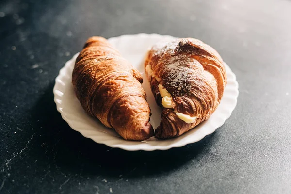 Avrupa kahvaltısı konsepti. Kremalı kruvasanlar beyaz tabakta ve siyah arka planda.
