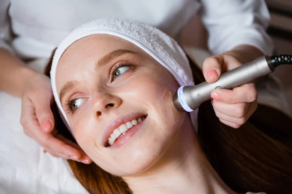 Primer plano. Chica pelirroja feliz en un procedimiento cosmético de cuidado de la piel. Dispositivos de cosmetología — Foto de Stock