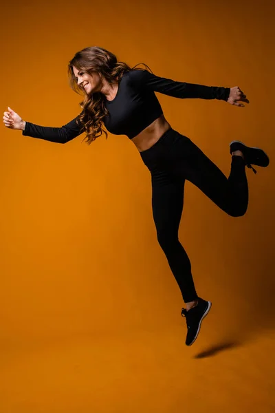 Белая девушка спортивного телосложения делает прыжок на оранжевом фоне. Счастливый тренер по фитнесу в прыжке, движении — стоковое фото