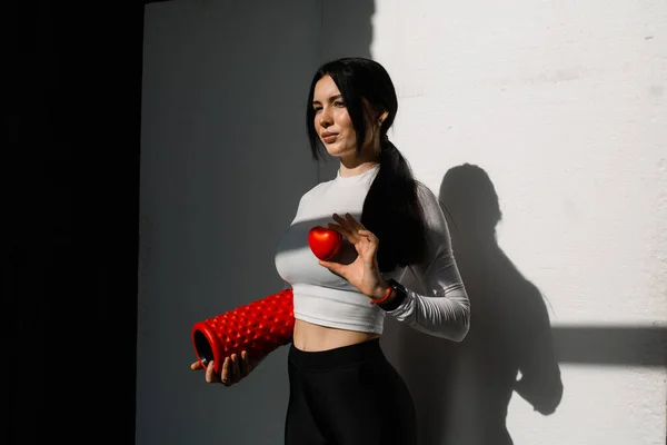 Девушка-тренер по пилатесу или физиотерапевтическим упражнениям держит в руке рулон массажа и красное сердце. Понятие здорового образа жизни — стоковое фото