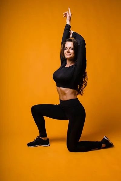 Kaukasiska flicka fitness tränare lungor på orange bakgrund — Stockfoto