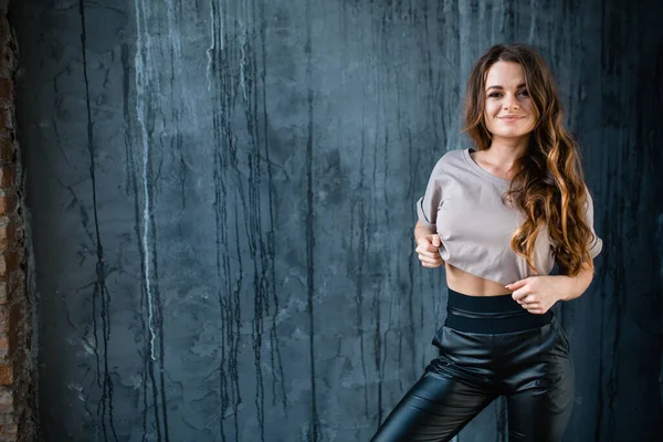 Caucasian girl in casual sportswear stands against the background of a gray wall in a loft studio. Sport and warm up