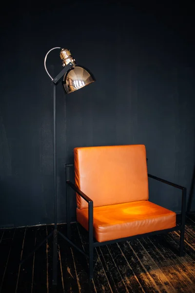 Ein orangefarbener Loft-Sessel auf schwarzen Metallbeinen an einer grauen Wand neben einer Designerstehlampe. Dachgeschossgestaltung — Stockfoto