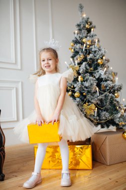 Şık giyinmiş bir çocuk yılbaşı ağacının yanında bir hediye kutusuyla duruyor. Noel konsepti