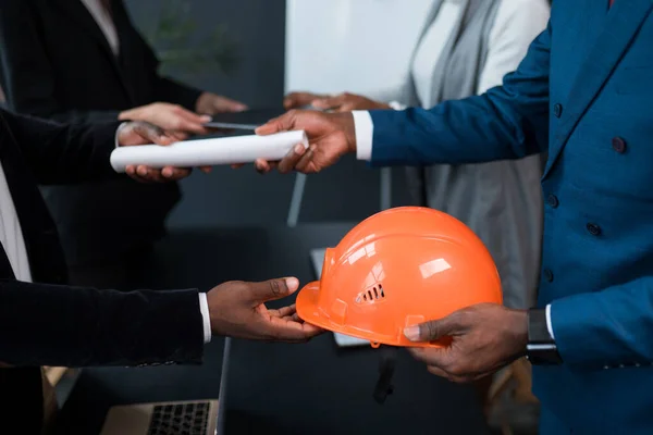 An African American man hands over a building permit and an orange construction helmet to an investor. The concept of business, construction, financing — Stock Photo, Image