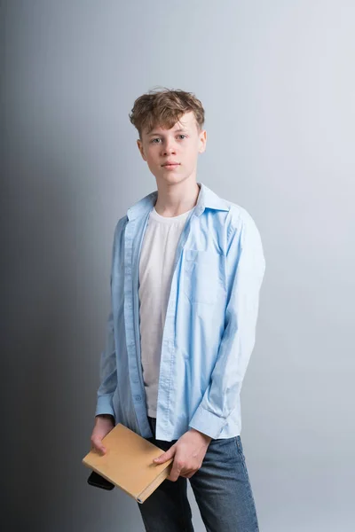 Młody atrakcyjny biały facet nastolatek w niebieski koszula i niebieski dżinsy stoi z pamiętnik w jego ręce na szary tło. — Zdjęcie stockowe