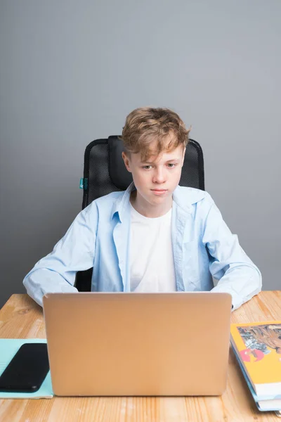 Um jovem estudante com uma camisa azul senta-se em uma aula on-line, em uma mesa esperando o início da lição no computador. Escolaridade durante a pandemia do coronavírus — Fotografia de Stock