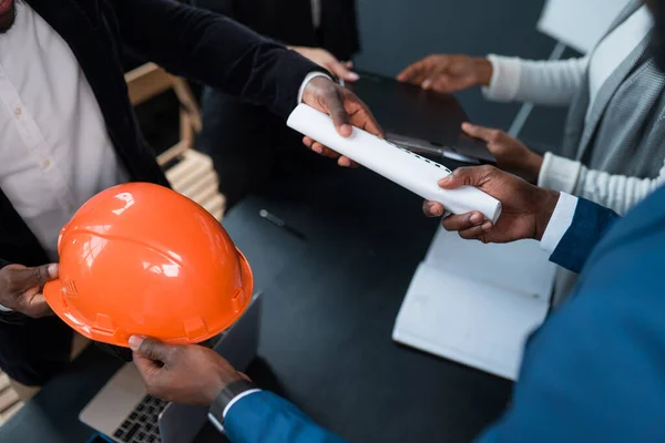 Афроамериканец передает инвестору разрешение на строительство и оранжевый строительный шлем. Концепция бизнеса, строительства, финансирования — стоковое фото