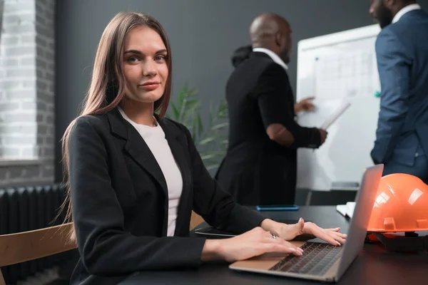 Европейка в деловом костюме сидит за рабочим столом с ноутбуком на деловой встрече с коллегами — стоковое фото
