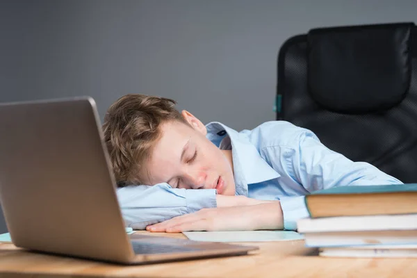 El niño de la escuela con una camisa azul duerme en un escritorio con una computadora portátil. El chico se quedó dormido en clase, cansado, aburrido en la escuela. aprendizaje en línea — Foto de Stock