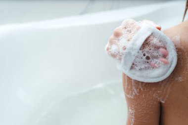 Kadınların omuzlarını yakın plan çek. Kız omzunu bir bez ile köpürüyor, banyoda oturuyor. Deri ve vücut bakımı. Rahatlama. kuşkonmaz prosedürleri