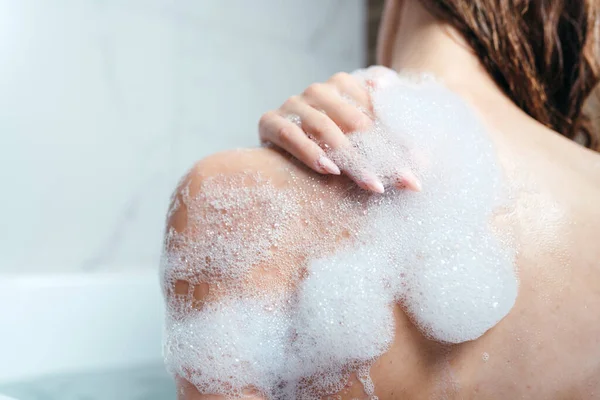 Primer plano de un hombro femenino en espuma. La chica se baña con espuma. Cuidado corporal, cuidado de la piel, procedimientos de espárragos — Foto de Stock
