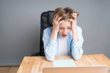 Liseli bir çocuk internet dersinde kafasını tutarak oturuyor. Evde eğitim, çalışmaktan yorulmak, koronavirüs salgını.