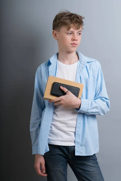 Młody atrakcyjny biały facet nastolatek w niebieski koszula i niebieski dżinsy stoi z pamiętnik w jego ręce na szary tło. — Zdjęcie stockowe