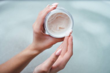 Pembe krem ya da bir kızın elindeki yüz maskesi. Bir kadın banyoda köpüğün arka planında bir kavanoz krema tutuyor. Spa prosedürü, vücut bakımı, cilt sağlığı ürünü