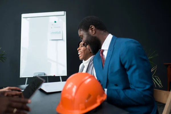 Мужчина и женщина-афроамериканец из крупной строительной компании сидят за рабочим столом с оранжевым строительным люком. — стоковое фото