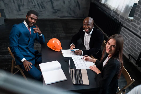 Os investidores de negócios afro-americanos sentam-se à mesa com um engenheiro e elaboram um plano de negócios. Reunião de negócios no escritório — Fotografia de Stock