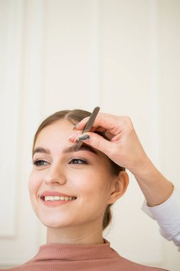 Hassas makyajlı güzel bir kıza kaşlarını yapması için cımbız verilir. Fazla kıllar alınıyor. Makyaj ve kozmetik konsepti.
