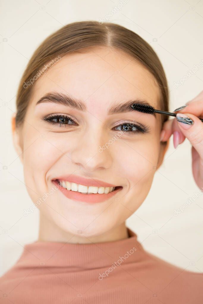 The master combs the eyebrows of a beautiful girl. Beautiful attractive girl smiling. Well-groomed girl with beautiful thick eyebrows, delicate makeup