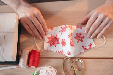 Yukarıdan bak. Noel Ağacı deseninde Noel Tatili Kapalı Maskesi dikmek. Tıbbi maskeli kadın ellerinin üst görüntüsü