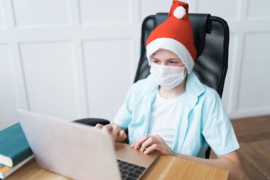 Tek kullanımlık yüz maskesi takan ve Noel Baba şapkası takan bir çocuk.