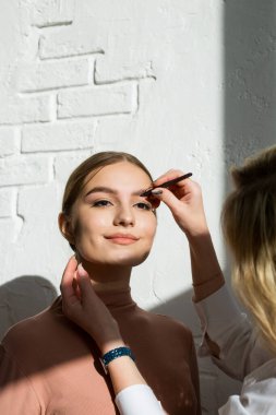 Makyaj ustası güzel bir kızın kaşlarını boyar. Kaş boyama ve şekillendirme prosedürü.
