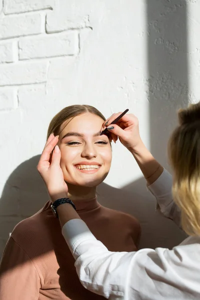 Master makes bushy eyebrows of a beautiful girl with an eyebrow dyeing brush. Eyebrow shaping, beautiful eyebrows, makeup — Stock Photo, Image