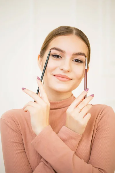 Girl apply a brush with a cosmetic product to her eyebrows. Beautiful cute girl smiles and makes eyebrow makeup — Stock Photo, Image