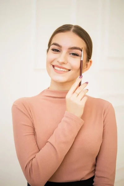 Chica aplicar un cepillo con un producto cosmético a sus cejas. Hermosa linda chica sonríe y hace maquillaje de cejas —  Fotos de Stock