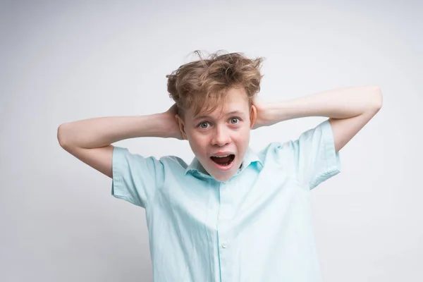 Um menino caucasiano está gritando com os ouvidos fechados pelas mãos — Fotografia de Stock