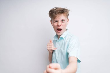 Beyaz arka planda mavi polo tişörtlü, iade edilmiş beyaz bir çocuk. Eğleniyor ve kameraya surat yapıyor.