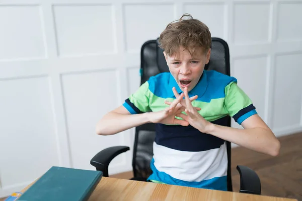 A mid shot of a tired Caucasian teenage boy yawning and stretching while sitting at the table during his online classes — Stock Photo, Image