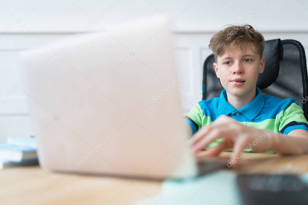 Cute Caucasian boy is nervous during the exam. He's studying online from home using his laptop. Online education concept