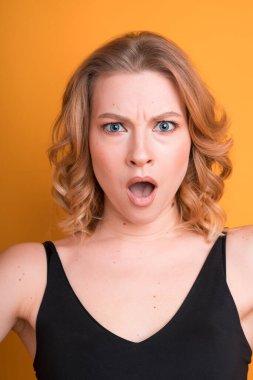 Ağzı açık, üzgün, genç, beyaz bir kızın portresi. Turuncu arka planda izole edilmiş. Duygular ve duygular