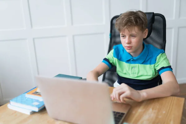 Menino europeu bonito está jogando jogos de computador em seu laptop com entusiasmo. Ele está a usar uma camisa de pólo listrada na moda. — Fotografia de Stock